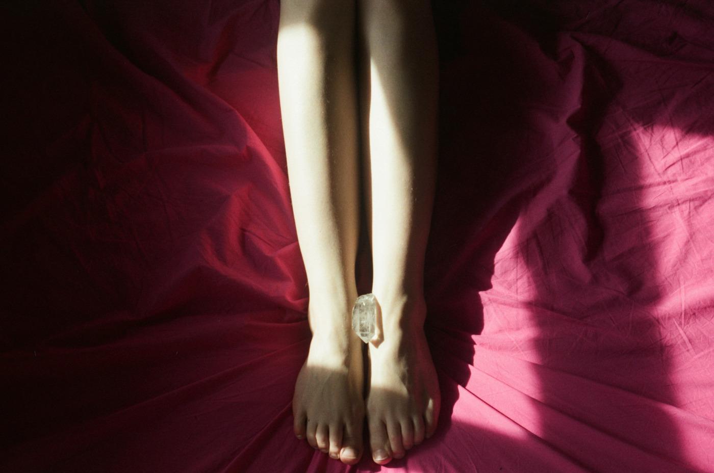 “a photoof a piece of crystal is placed between a woman’s feet who is in bed on red bedsheets from Lina Scheynius photo-essay for Tabayer jewelry Tabayer jewellery”